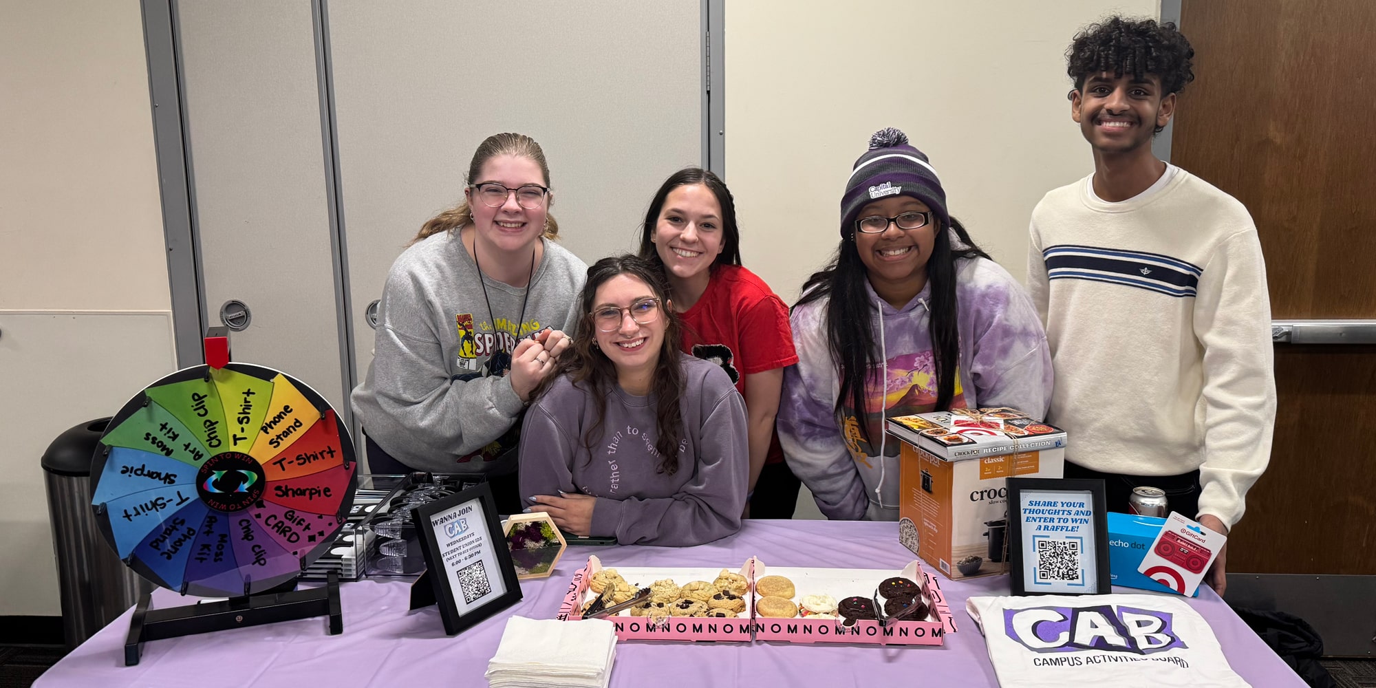 A group of students in CAB sit behind a welcome table smiling